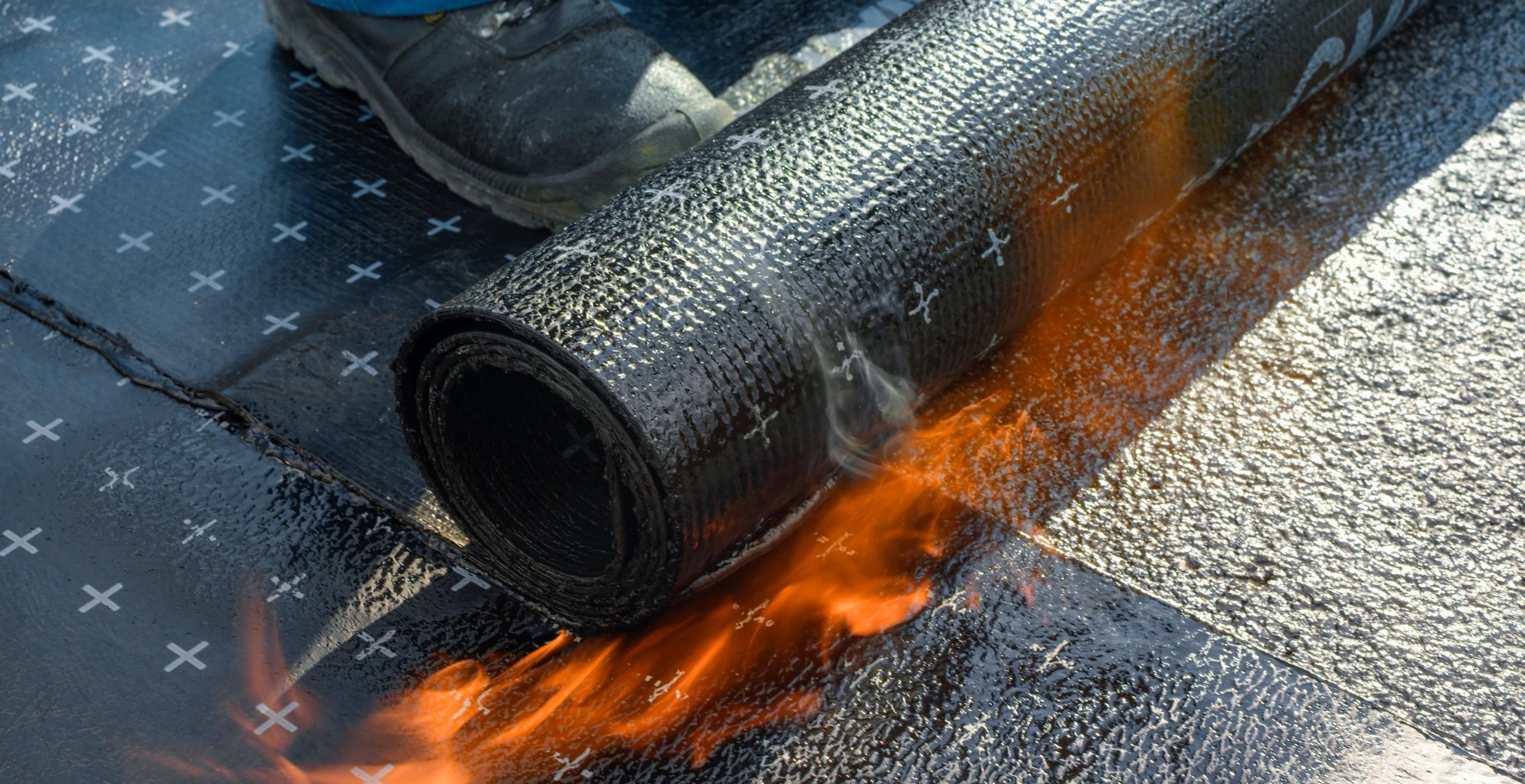 Technician heating and melting bitumen rolls during torch-on membrane installation