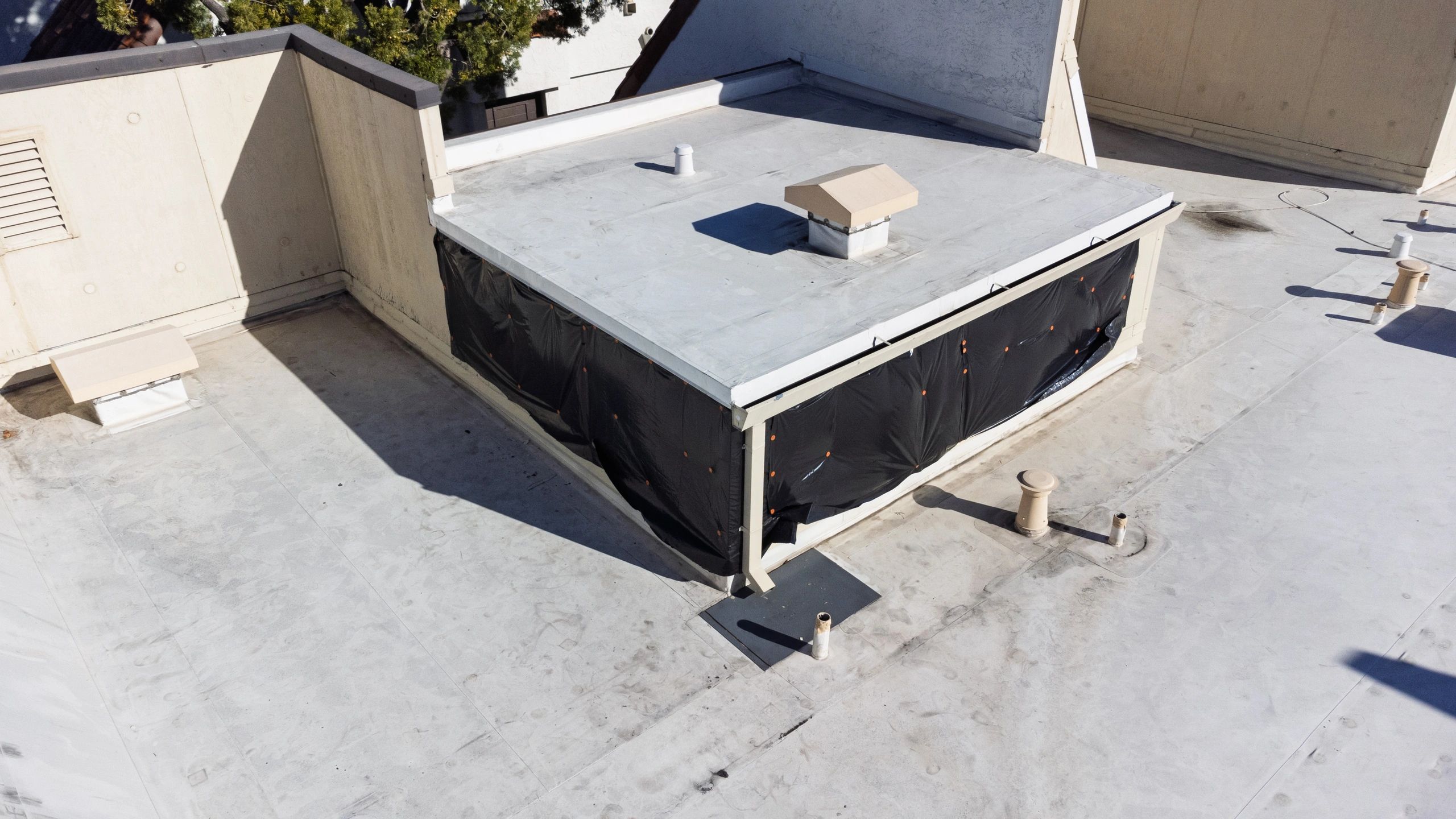 Commercial flat roof area temporarily protected with black sheeting around penetrations